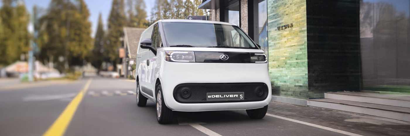 Weißer Elektro-Lieferwagen eDeliver 5 auf einer Stadtstraße, umgeben von modernen Gebäuden und Bäumen.