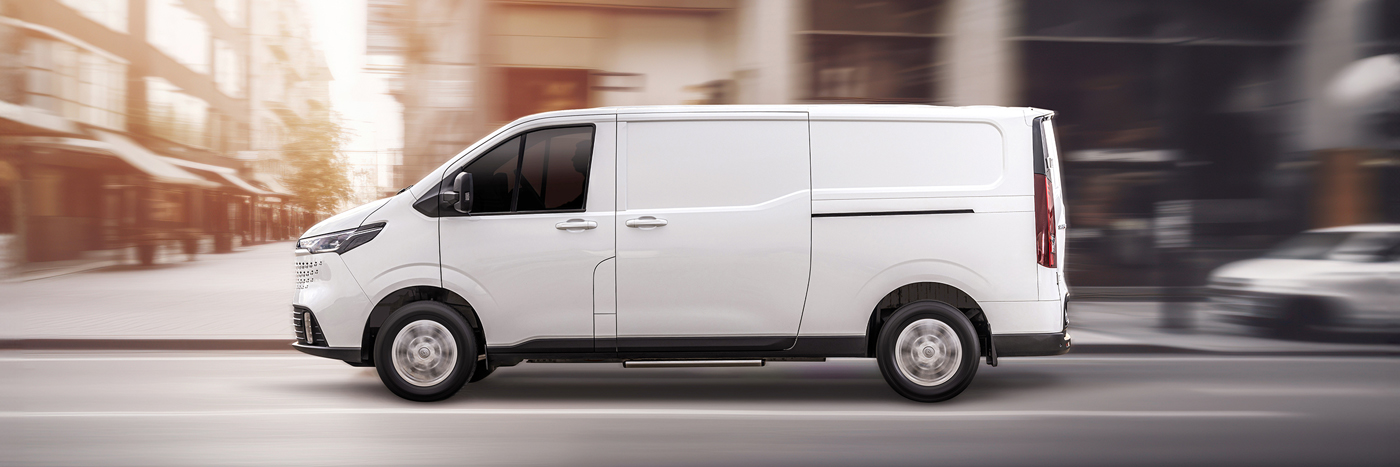 Weißer Lieferwagen fährt auf einer Stadtstraße, umgeben von urbaner Architektur.