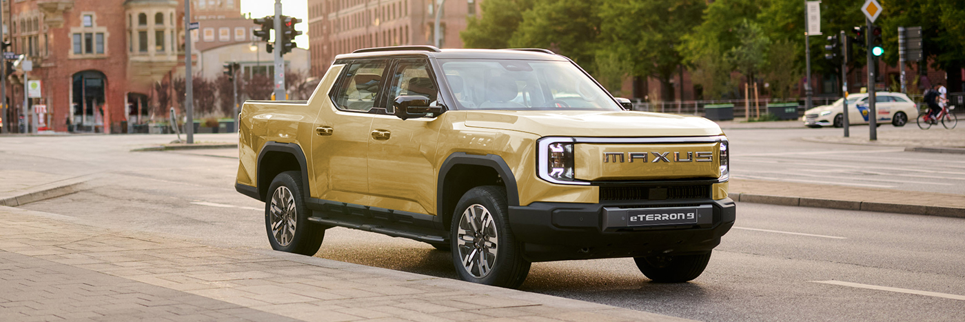 Ein gelber Maxus ET5 Pickup fährt auf einer Stadtstraße mit modernen Gebäuden im Hintergrund.