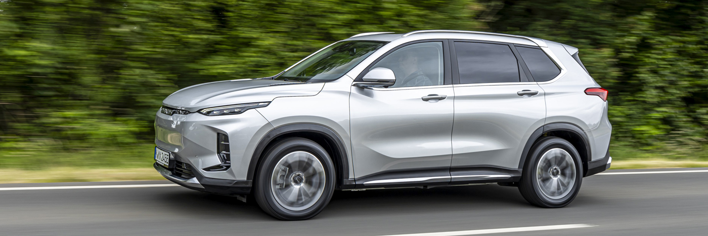 Ein silberner SUV fährt auf einer Landstraße, umgeben von grüner Landschaft.